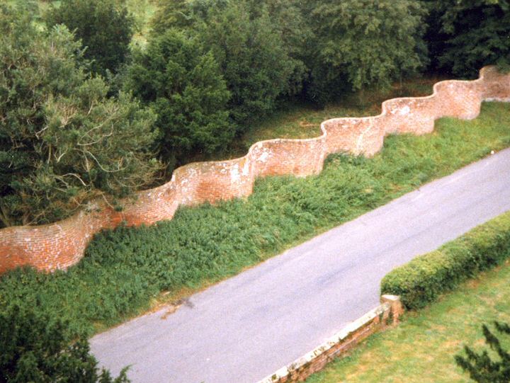 The Crinkle Crankle wall in Walpole Road, Bramfield, viewed from the Church tower opposite, shortly after the wall was cleaned and re-pointed in the late 1990's. These walls, fashioned in curves and visually very pleasing, are an East Anglian feature. The curving, it is said, gives strength plus plantings benefit from the warmth and shelter.  