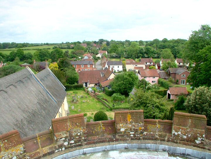 Looking due South from the tower of St.Andrew's church in the centre of Bramfield towards the back of the Queen's Head public house and the crossroads. The thatched roof of the Church is on the left, seemingly close but actually detached from the ancient tower. Note the initials carved into the tower bricks. The A144 main road is out of sight but runs horizontally across the middle of the picture. The lane clearly visible is wending its way past the village hall and school, eastwards to Wenhaston just two miles away.   